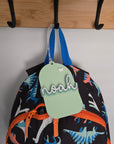 Colorful backpack with dinosaur pattern and 'noah' tag hanging on a wooden rack.