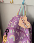 Purple bag with rainbow patterns and a name tag on a light gray background
