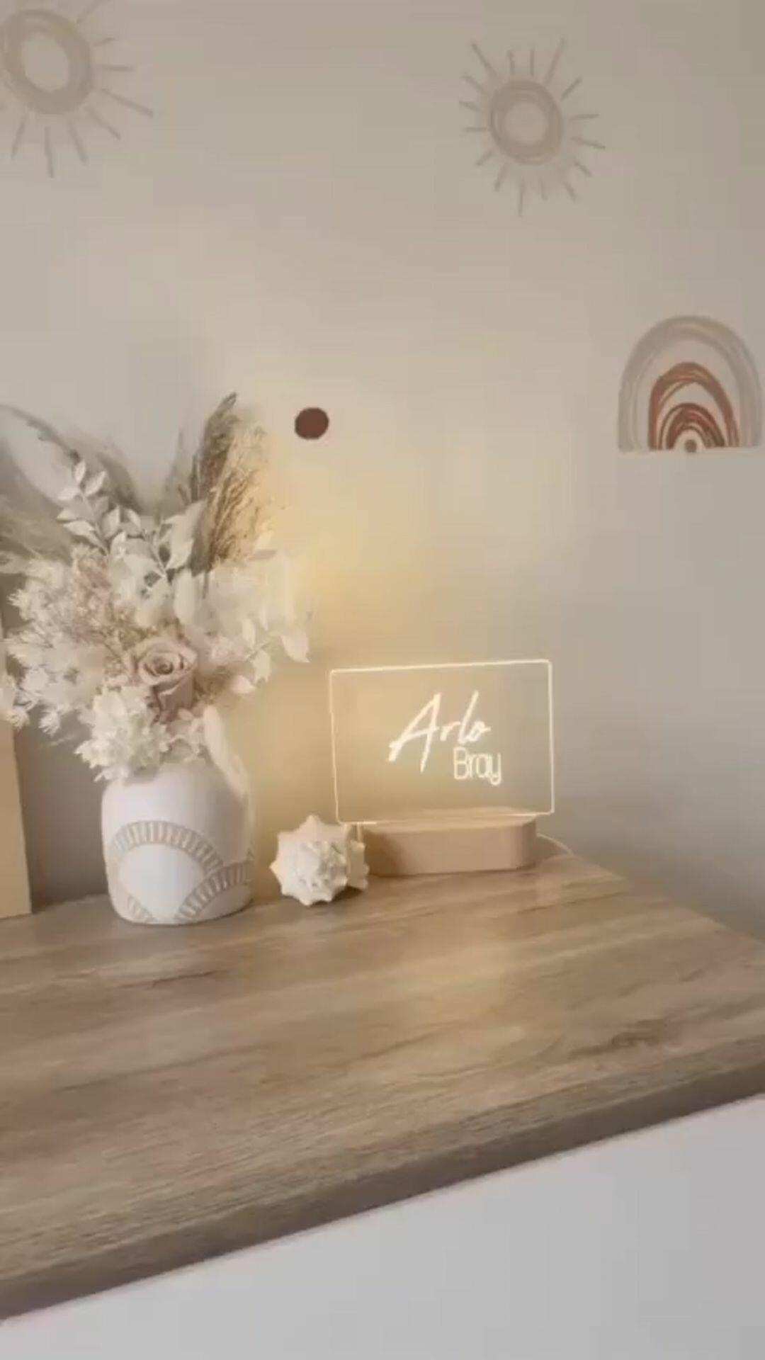 A serene and stylish nursery display featuring a personalized Warm White Night Light in the Dual Signature design. The light glows gently, showcasing the names