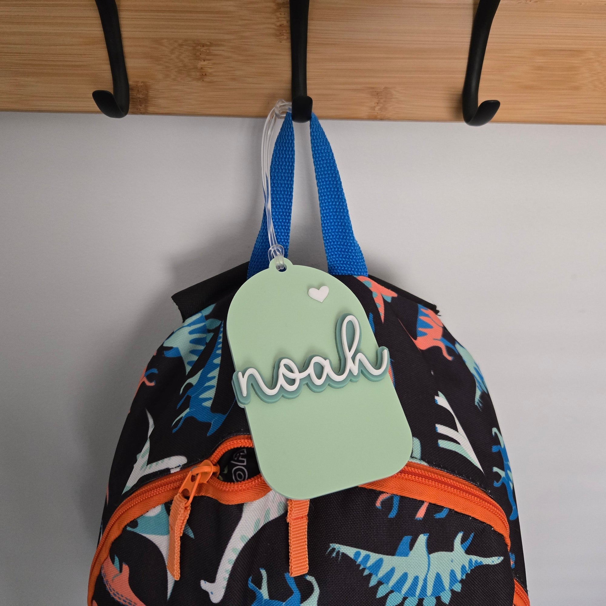 Colorful backpack with dinosaur pattern and 'noah' tag hanging on a wooden rack.
