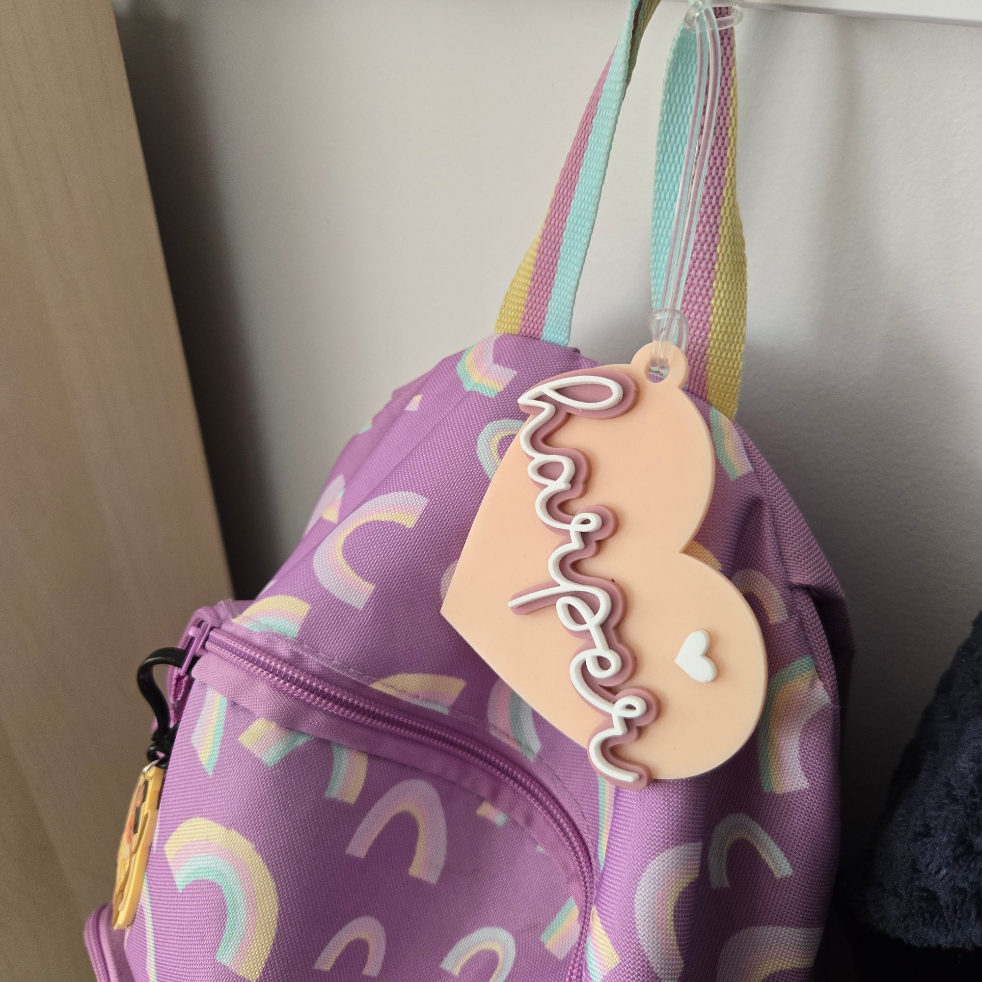 Purple bag with rainbow patterns and a heart-shaped name tag on a white surface.