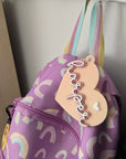 Purple bag with rainbow patterns and a heart-shaped name tag on a white surface.
