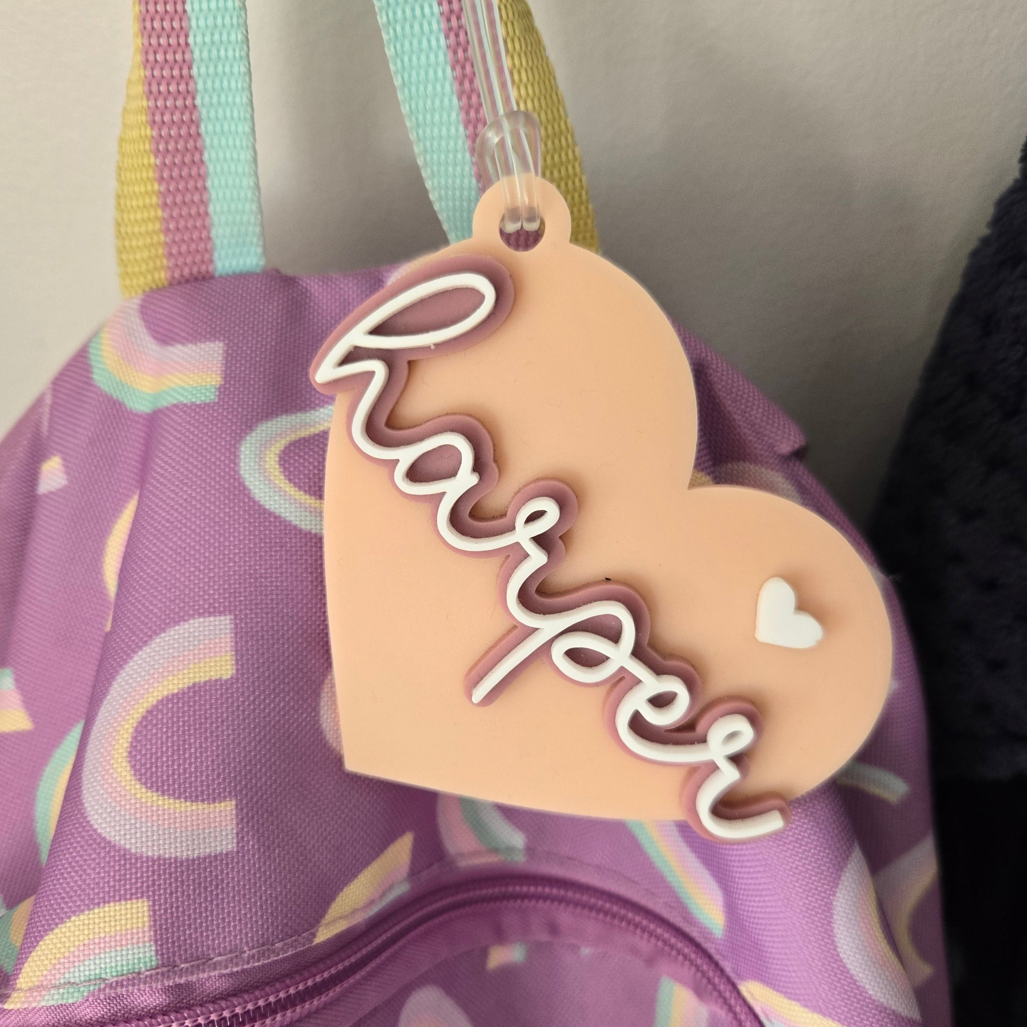 Heart-shaped name tag with 'Harper' on a purple bag with rainbow patterns