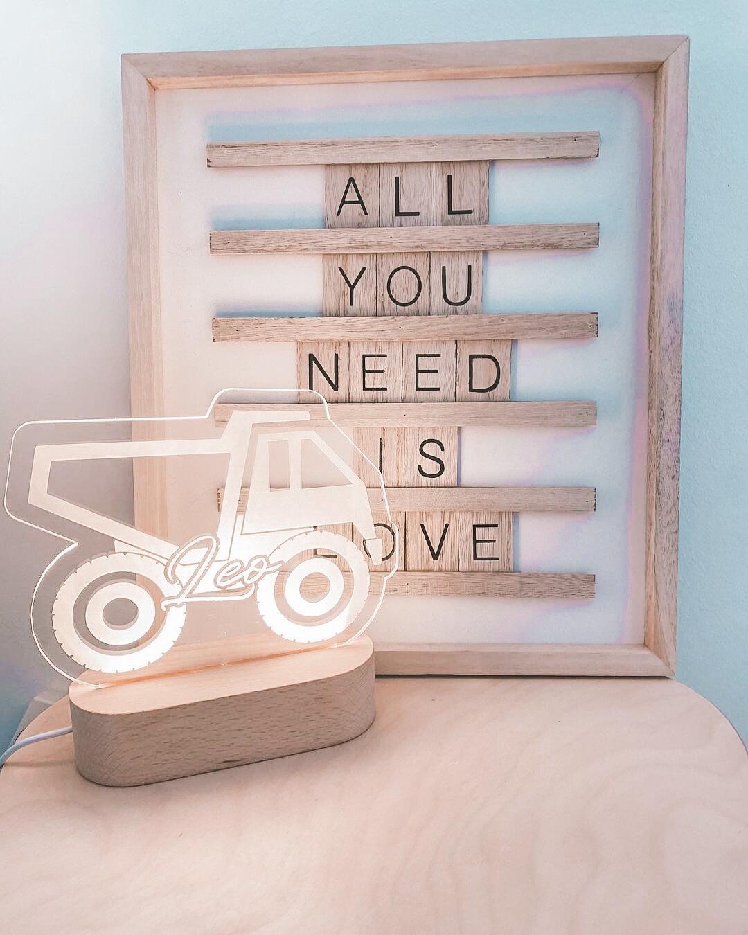 A playful nursery scene featuring a personalized Warm White Night Light by The Willow Corner in the Construction Truck design. The light glows warmly, displaying the name 